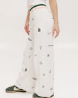 A pair of white Kennedy pants with a checkered print and embroidered icons, displayed on a model.