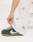 A pair of white Kennedy pants with a checkered print and embroidered icons, displayed on a model.