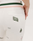 A pair of white Kennedy pants with a checkered print and embroidered icons, displayed on a model.