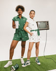 Two women wearing a green and white romper with embroidered golf icons, a tie belt at the waist, and cuffed sleeves.