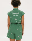 A woman wearing a green romper with embroidered golf icons, a tie belt at the waist, and cuffed sleeves.