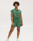 A woman wearing a green romper with embroidered golf icons, a tie belt at the waist, and cuffed sleeves.
