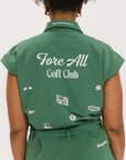 A woman wearing a green romper with embroidered golf icons, a tie belt at the waist, and cuffed sleeves.