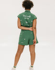A woman wearing a green romper with embroidered golf icons, a tie belt at the waist, and cuffed sleeves.