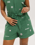 A woman wearing a green romper with embroidered golf icons, a tie belt at the waist, and cuffed sleeves.