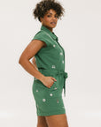 A woman wearing a green romper with embroidered golf icons, a tie belt at the waist, and cuffed sleeves.