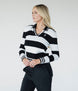 A woman wearing a black and white striped sweater with a V-neck collar and a small embroidered patch on the left chest.