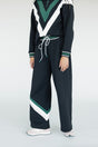 A model wearing a black sweatpant with green and white stripe details, paired with a matching sweatshirt.