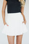 A woman wearing a white high-waisted skirt with built-in shorties and side seam pockets, paired with a black top.