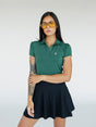 A woman wearing a green polo shirt with a collar, featuring a four-button placket and puff sleeves, paired with a black skirt.