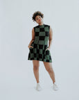 A woman wearing a green checkered sleeveless golf dress with a mock neck, paired with white socks and checkered shoes.