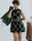 A woman wearing a green checkered sleeveless golf dress with a mock neck, paired with white socks and checkered shoes.