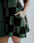 A woman wearing a green checkered sleeveless golf dress with a mock neck, paired with white socks and checkered shoes.