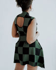 A woman wearing a green checkered sleeveless golf dress with a mock neck, paired with white socks and checkered shoes.