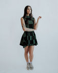 A woman wearing a green checkered sleeveless golf dress with a mock neck, paired with white socks and checkered shoes.
