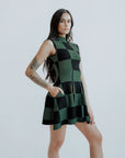 A woman wearing a green checkered sleeveless golf dress with a mock neck, paired with white socks and checkered shoes.