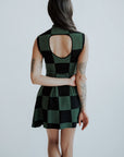 A woman wearing a green checkered sleeveless golf dress with a mock neck, paired with white socks and checkered shoes.