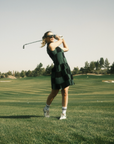 A woman wearing a green checkered sleeveless golf dress with a mock neck, paired with white socks and checkered shoes.