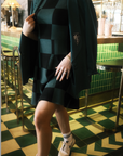 A woman wearing a green checkered sleeveless golf dress with a mock neck, paired with white socks and checkered shoes.